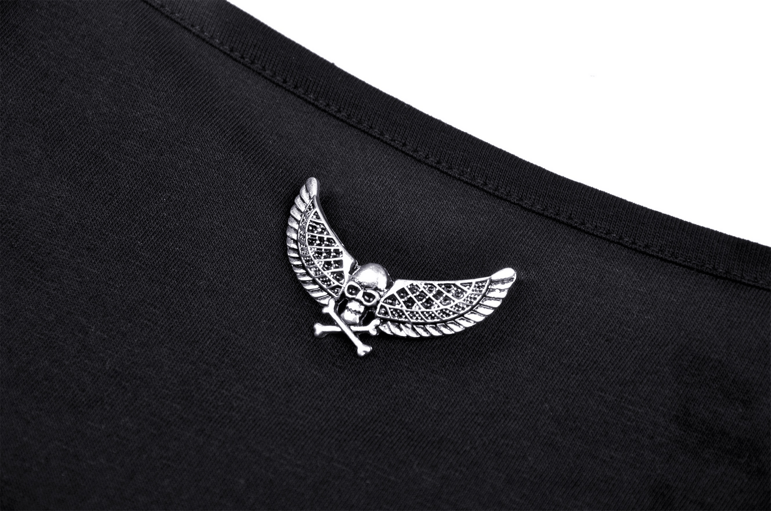 Close-up of a metal skull and wing embellishment on a dark gothic halter top, showcasing edgy fashion details.
