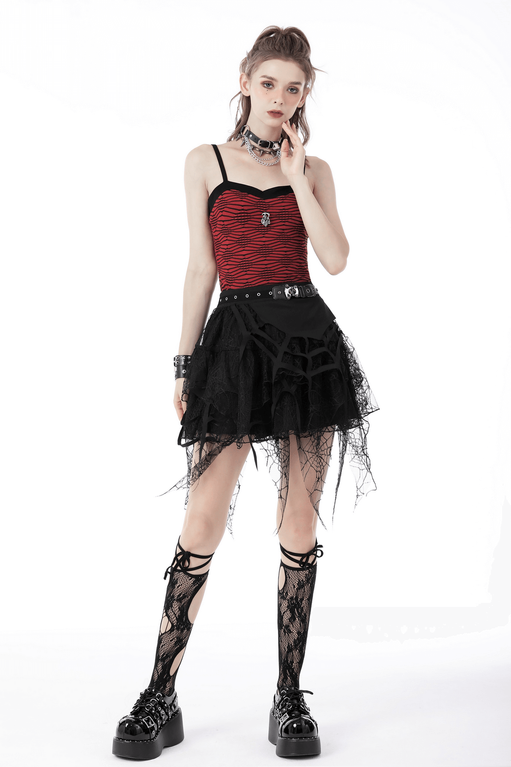 Model wearing a black lace mini skirt with spiderweb design, red top, and edgy accessories, showcasing gothic fashion.