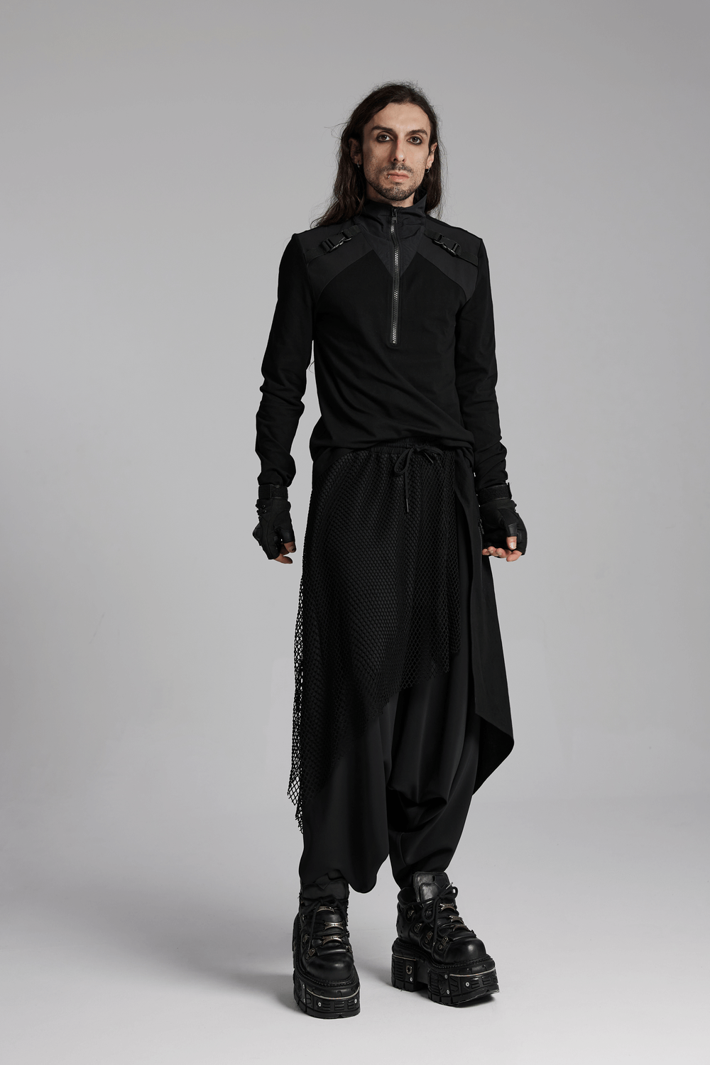 Dark punk streetwear look featuring a model in loose-fit harem pants and a black zip-up top with mesh accents.