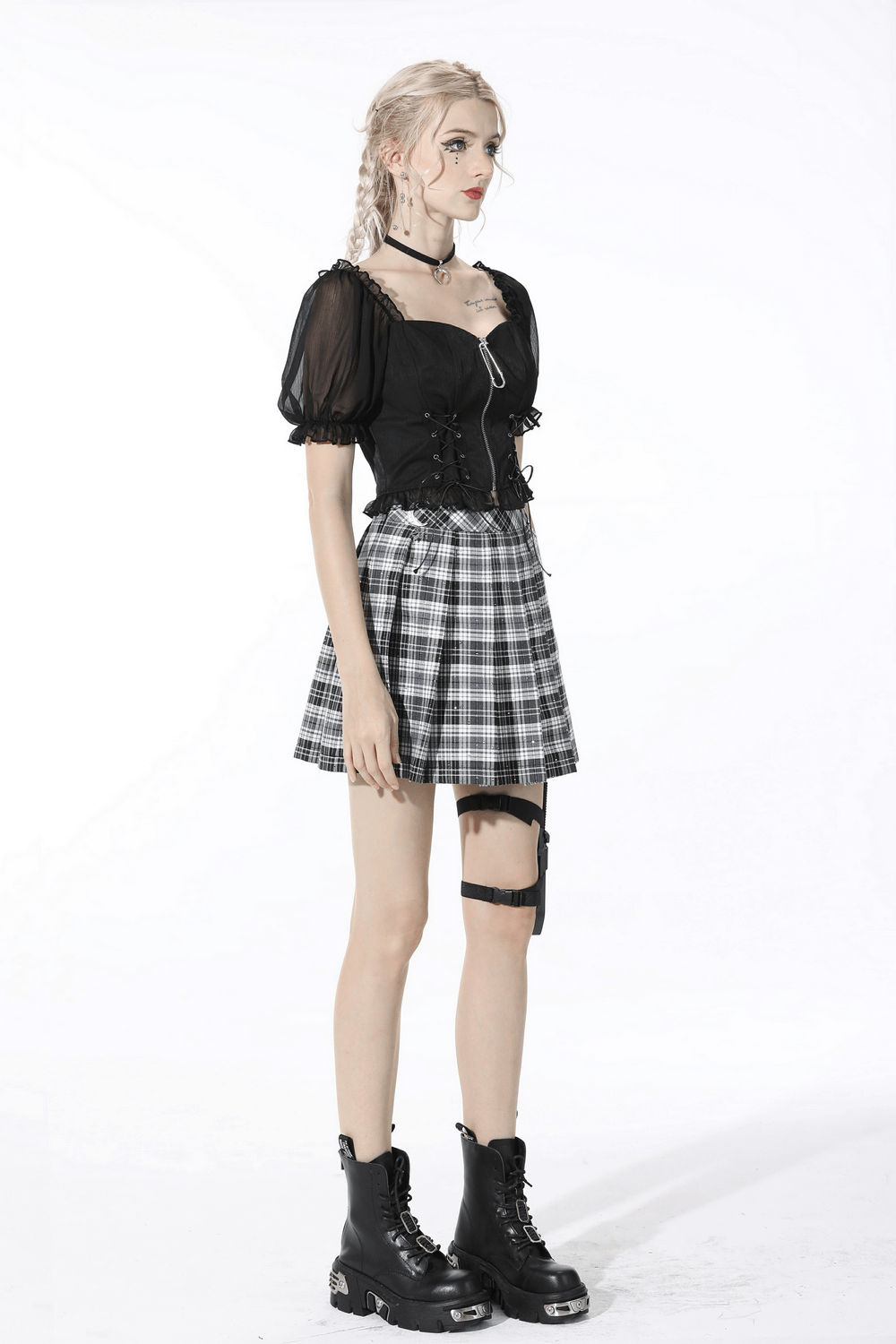 Edgy model in black crop top and plaid skirt, showcasing gothic style with lace-up detailing and chunky boots.