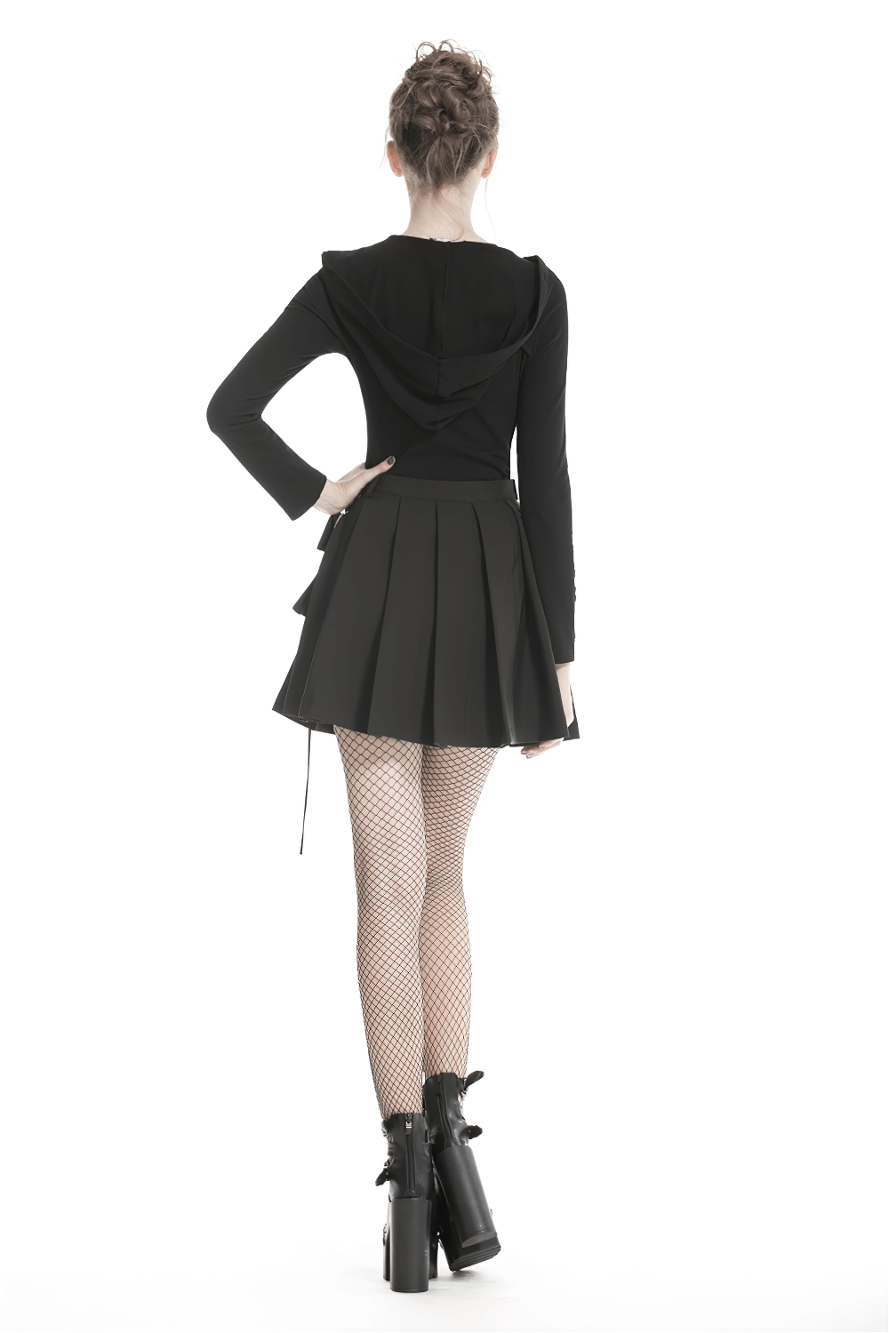Back view of a model in a black pleated mini skirt with a hooded top and fishnet tights, showcasing edgy punk fashion.