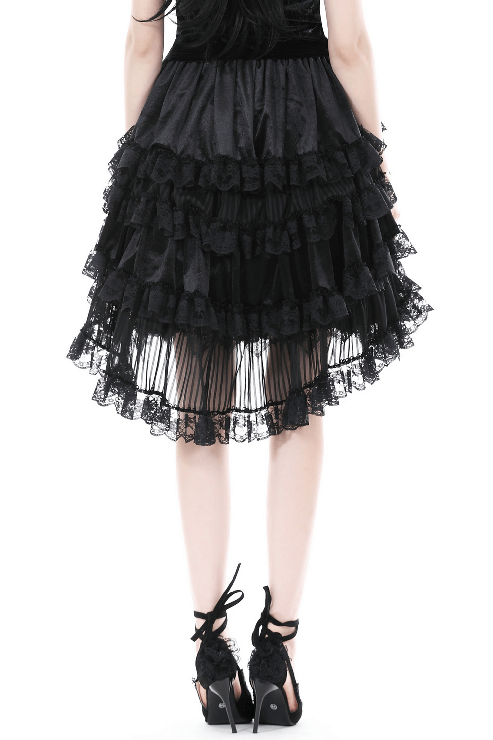 Back view of a dark romantic high-low black lace skirt with ruffles, paired with stylish black heels.