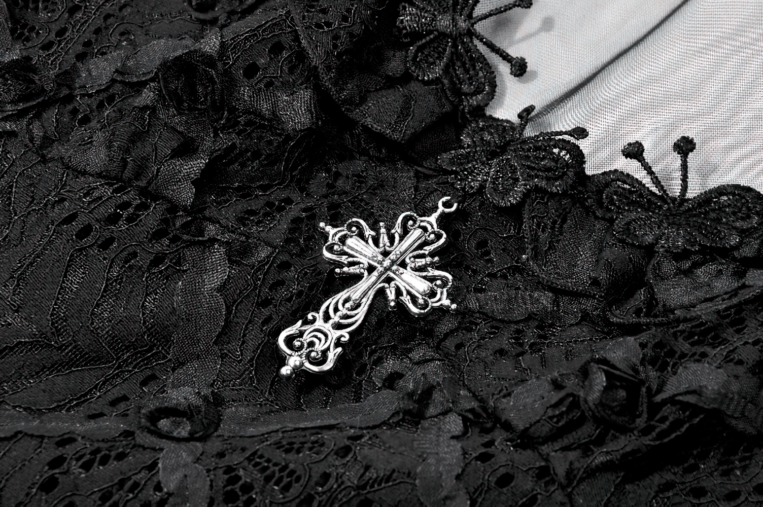 Close-up of decorative silver cross on Dark Romantic Lace Mini Dress with Corset Waist and Cross, showcasing delicate lace detail.
