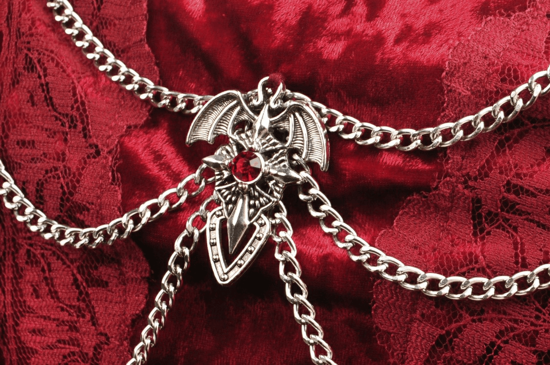 Dramatic silver chain with a bat and gemstone detail against deep red velvet fabric.