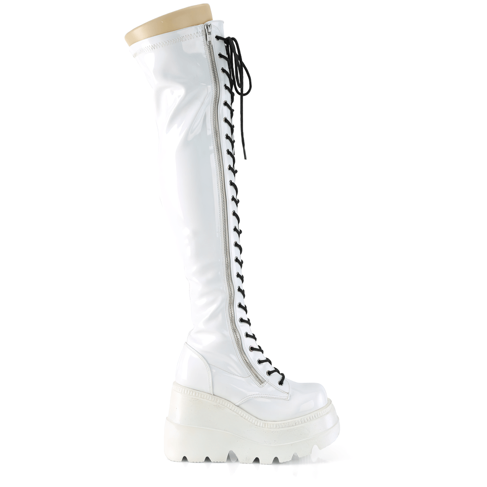 Demonia iridescent white thigh-high lace-up wedge boots with zipper, featuring shiny holographic finish and 4.5-inch platform.