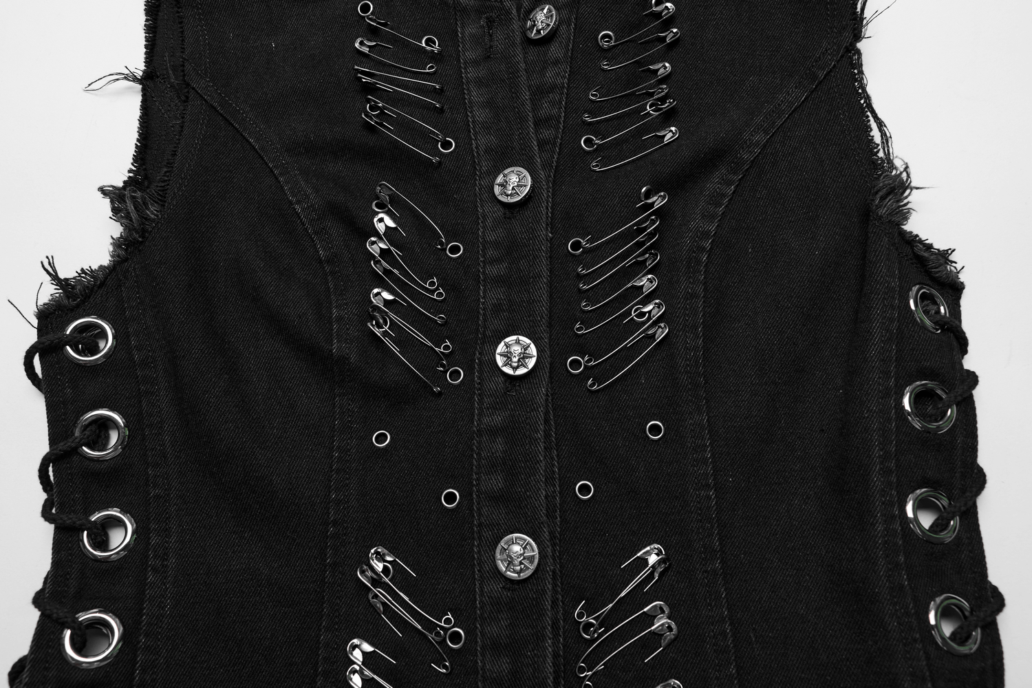 Close-up of a denim vest featuring punk safety pins and grommet details, showcasing edgy, raw fashion style.