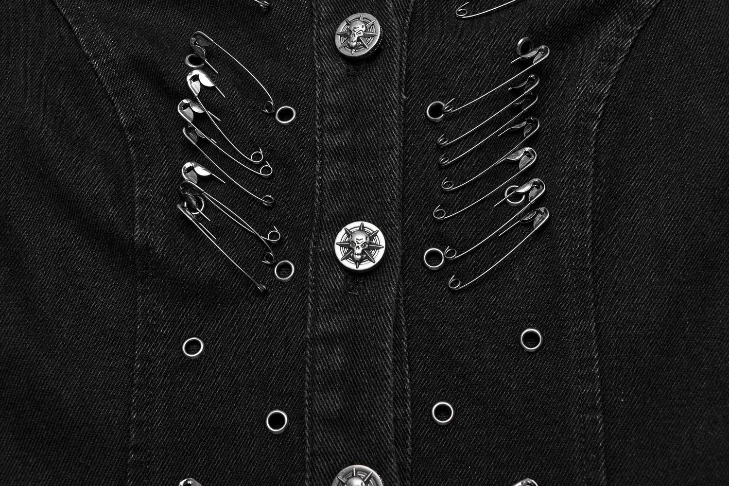 Close-up of punk-style black denim jacket featuring edgy safety pins and decorative buttons.