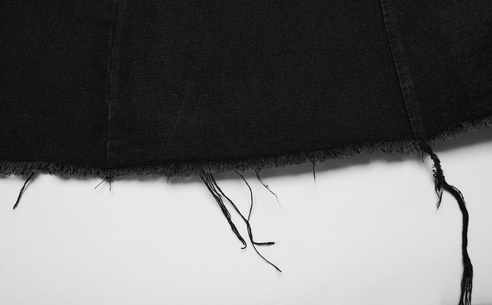 Close-up of the frayed hem detail on a black denim cape, showcasing raw edges and punk-inspired style.