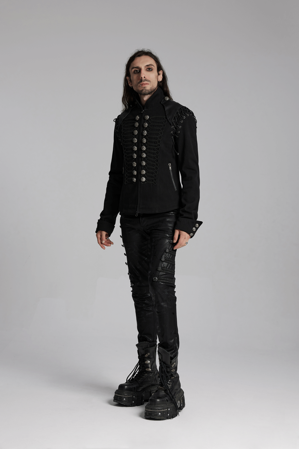 Edgy man in a detachable sleeved punk military jacket with vintage buttons and black pants, showcasing bold style.