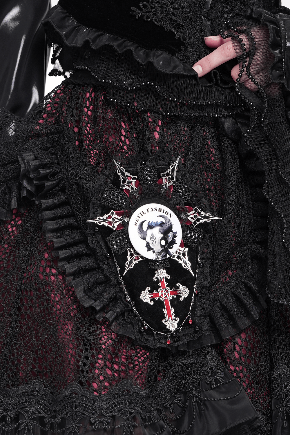 Gothic fashion detail featuring Devil Fashion horned skull logo badge on a ruffled black lace skirt.
