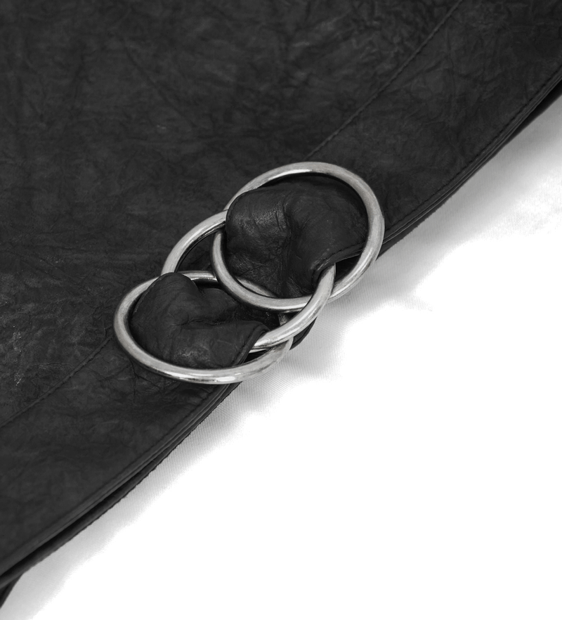 Close-up of silver metal rings on a black leather fabric, showcasing stylish detail of a men's kilt skirt.