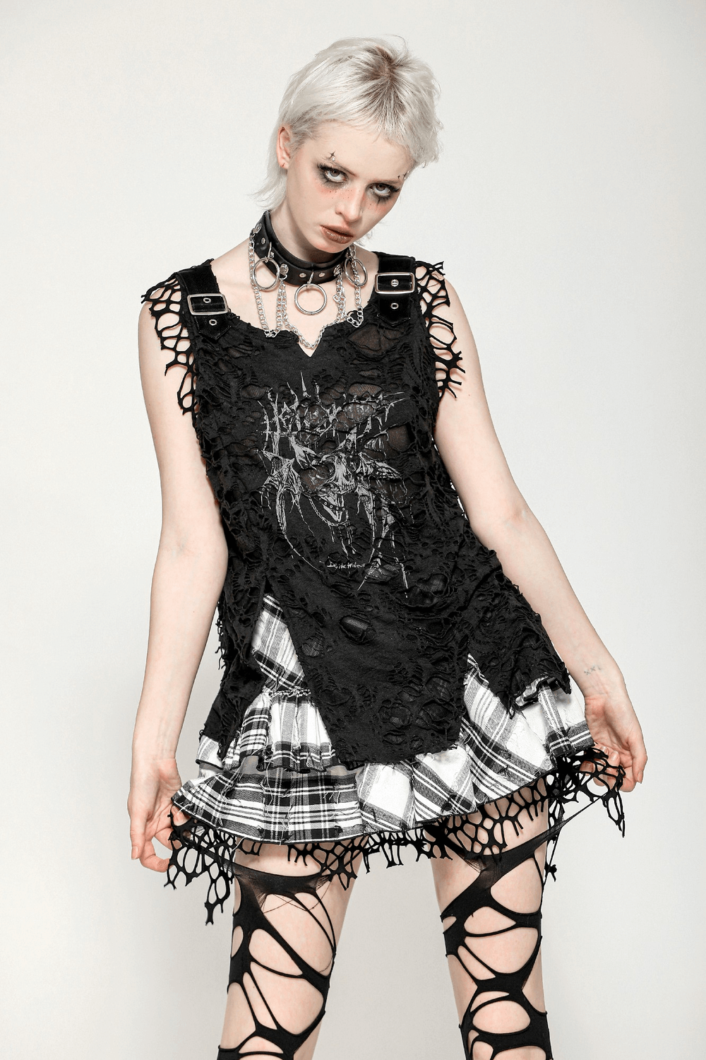 Gothic sleeveless black punk tank top with skull print and buckles, styled with ripped net and plaid skirt.
