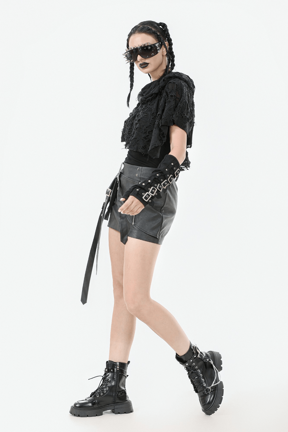 Trendy model wearing a distressed punk hooded poncho cape with tattered design, paired with edgy leather shorts and boots.