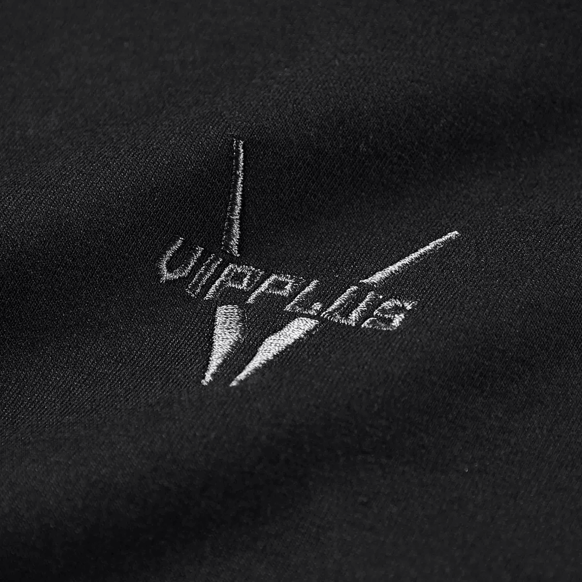 Close-up of embroidered logo on black fabric, featuring sleek design for a stylish alternative fashion touch.