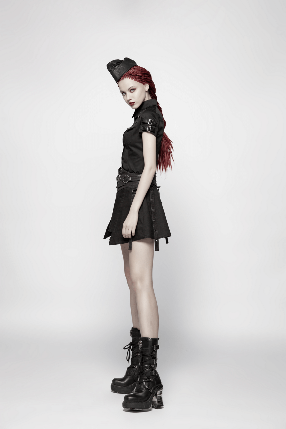 Model in stylish black tactical dress with buckles and combat boots, showcasing edgy fashion and confident pose.