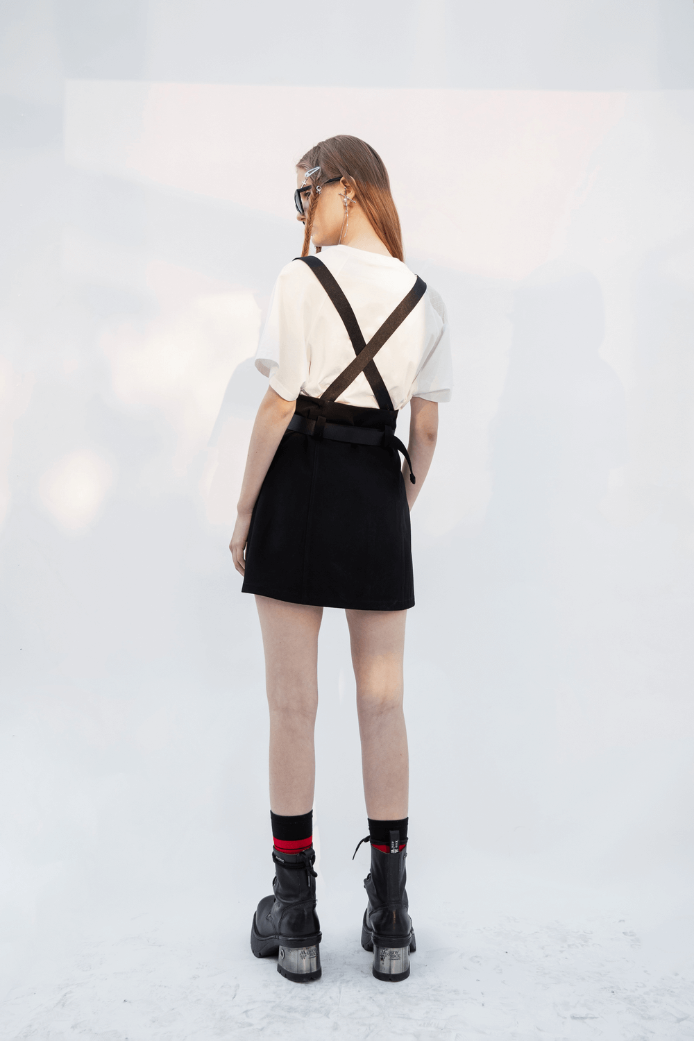 Model showcasing edgy A-line mini skirt with detachable chain straps, paired with stylish boots, from the back view.