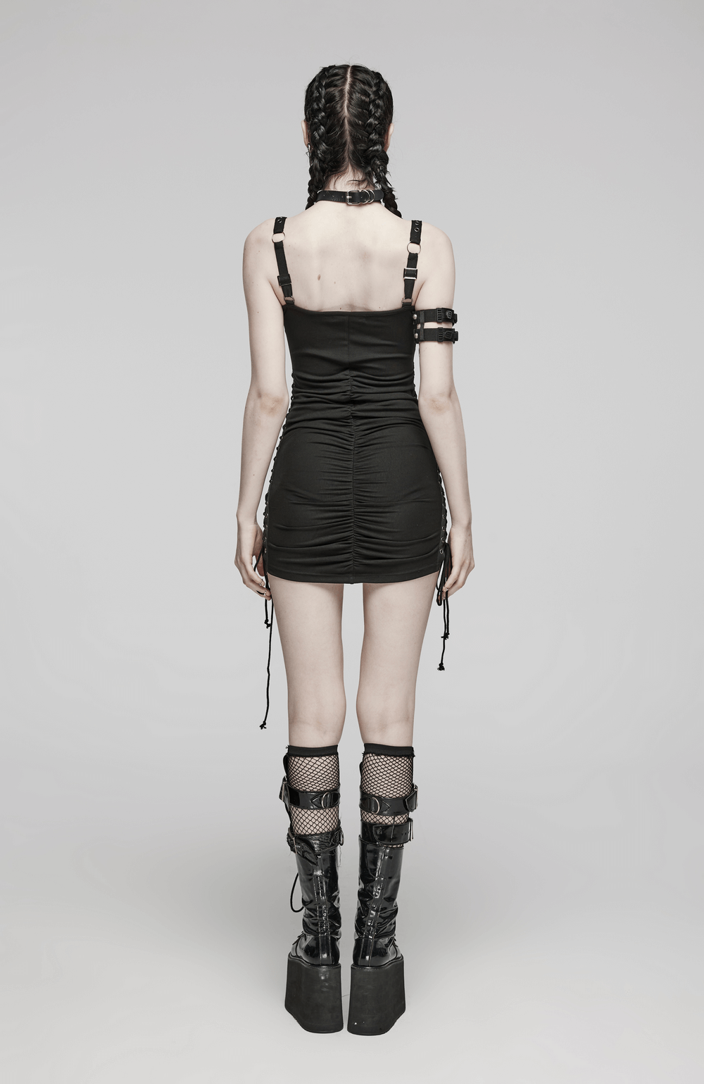 Back view of a model in a black adjustable mini dress with eyelet straps and stylish knee-high chunky boots.