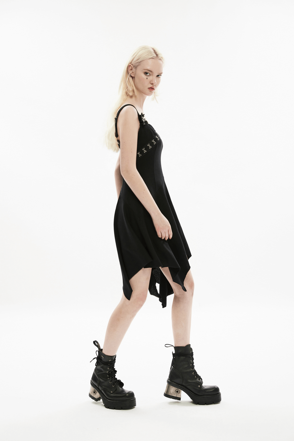 Model wearing an edgy asymmetrical black dress with a detachable brooch and stylish platform boots.