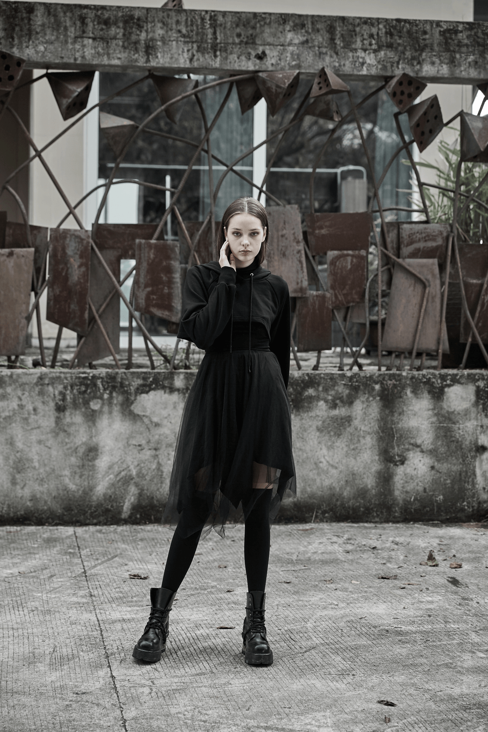 Stylish model in an edgy black crop hoodie, tulle skirt, and combat boots, posing confidently outdoors.