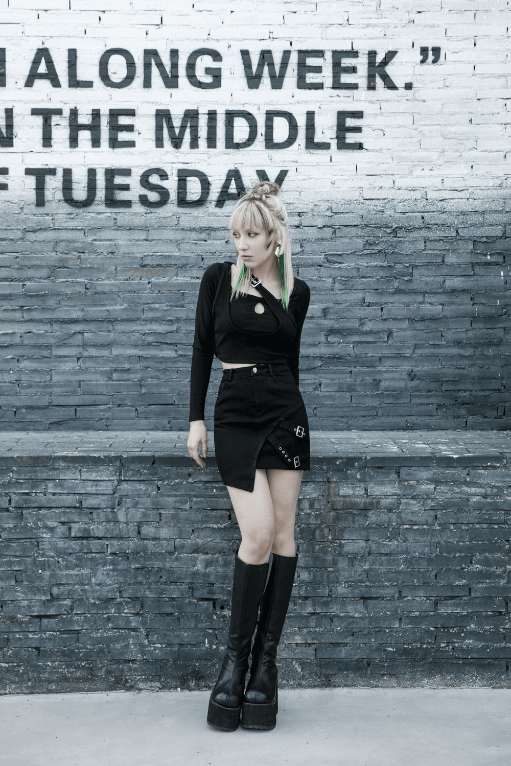 Edgy black denim mini skirt with buckle detail, styled with a cropped top and platform boots, standing against a graffiti wall.