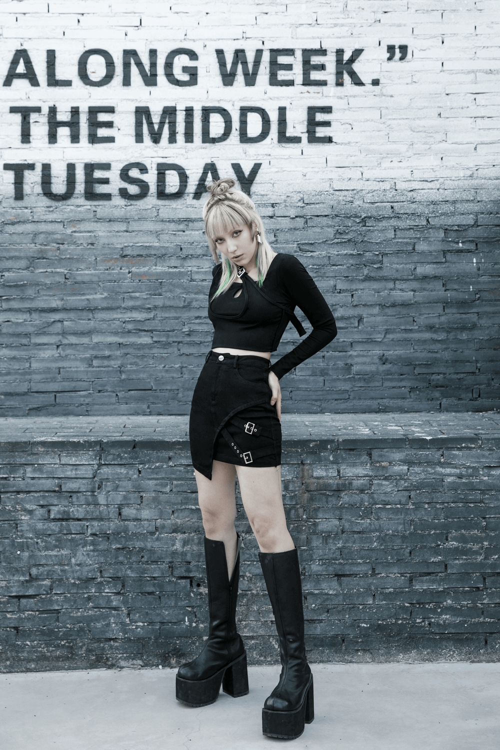 Edgy black denim mini skirt with buckle detail, styled with a cropped top and platform boots against a urban backdrop.