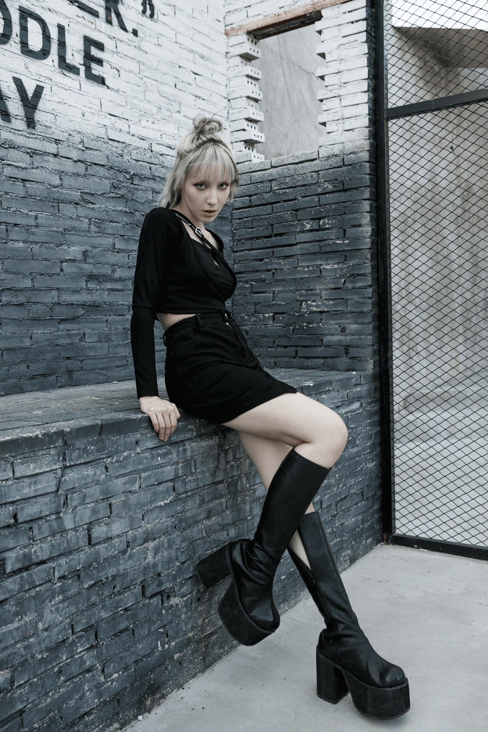 Edgy black denim mini skirt with buckle detail paired with knee-high platform boots, styled against an urban backdrop.