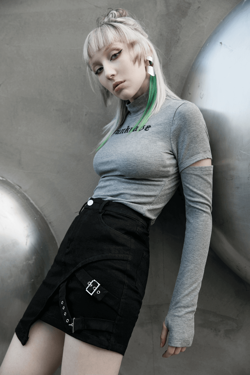 Edgy black denim mini skirt with buckle detail, styled with a fitted gray long-sleeve top and unique accessories.