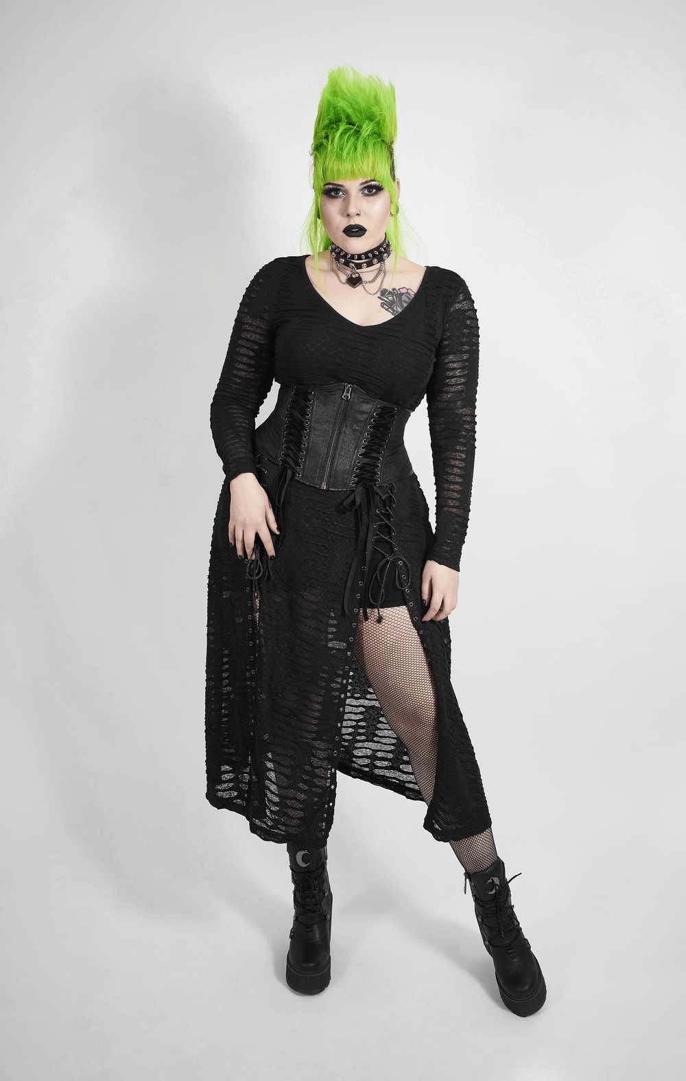 Model showcases an edgy black gothic corset belt with lace-up details, styled with a layered black outfit and vibrant green hair.
