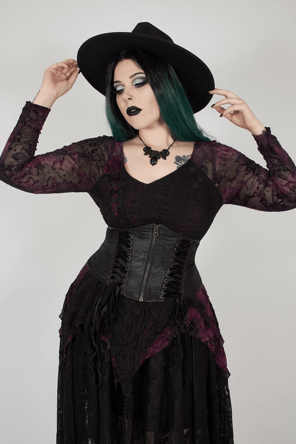 Gothic model wearing an edgy black lace corset belt with lace-up details and wide-brimmed hat, embracing dark fashion.