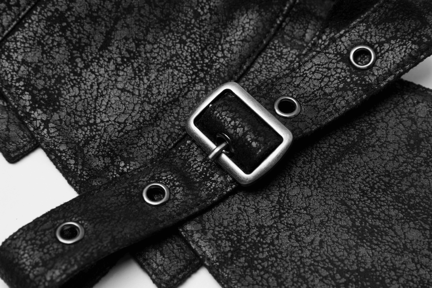 Close-up of black leather vest strap with buckle and grommets, showcasing edgy style and craftsmanship.