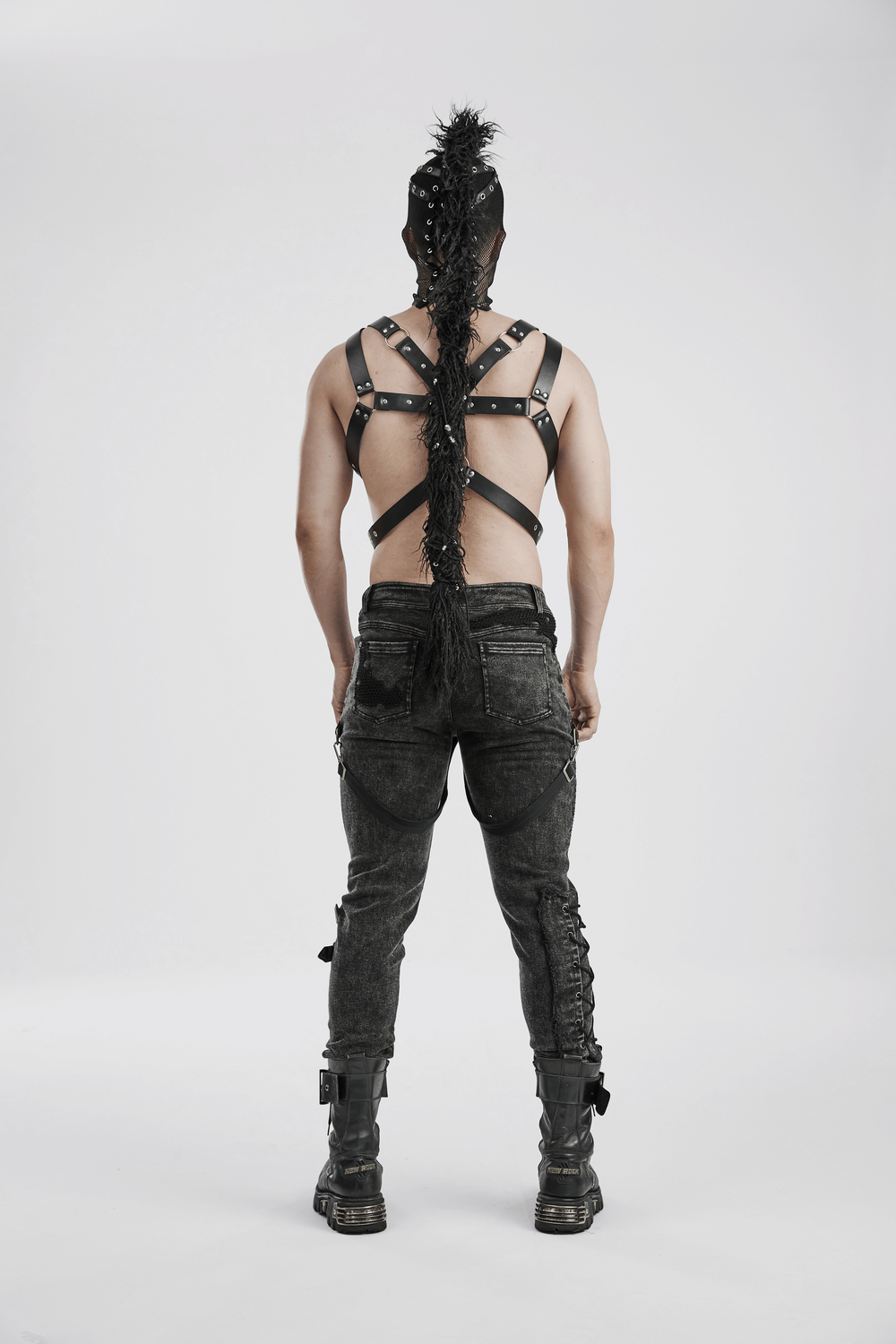 Back view of a man in punk style with a black mesh hood, mohawk ponytail, and strappy outfit showcasing edgy fashion.