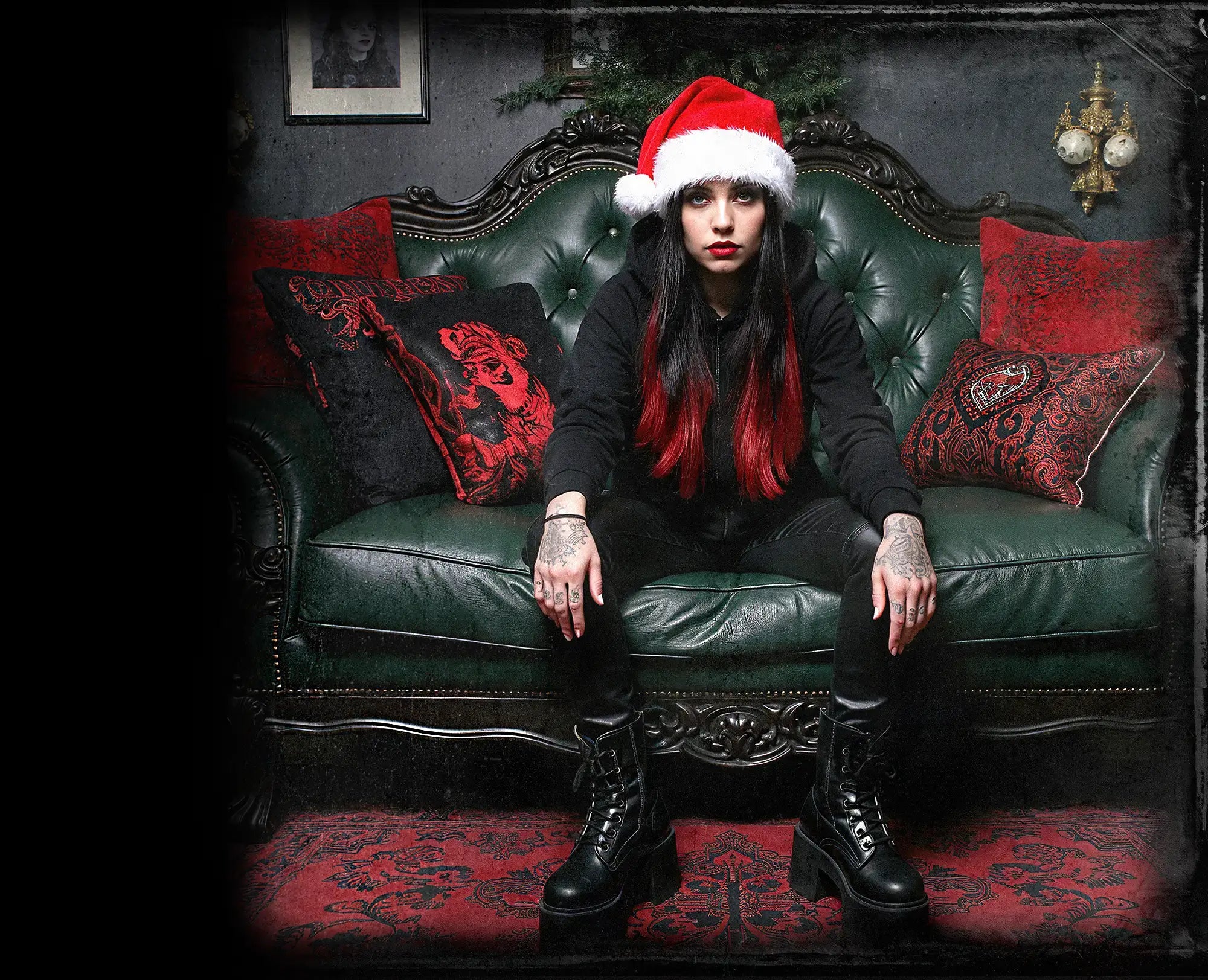 Stylish woman with red-tipped hair and a Santa hat sitting on a vintage green sofa, surrounded by festive decor, perfect for alternative Christmas 2024 themes.