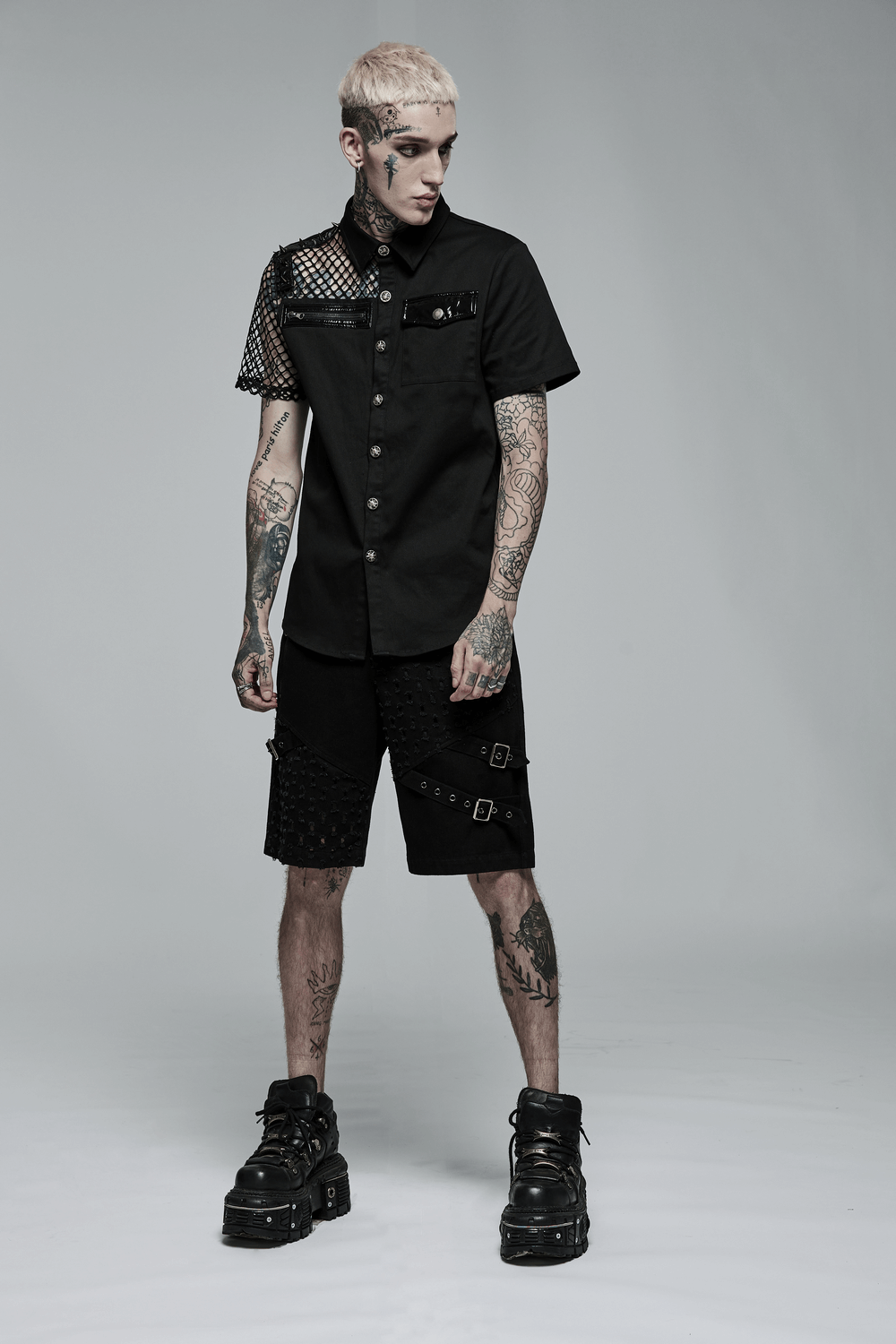 Edgy punk model wearing a fishnet sleeves button-up gothic shirt with asymmetrical stitching and shorts, showcasing alternative fashion.