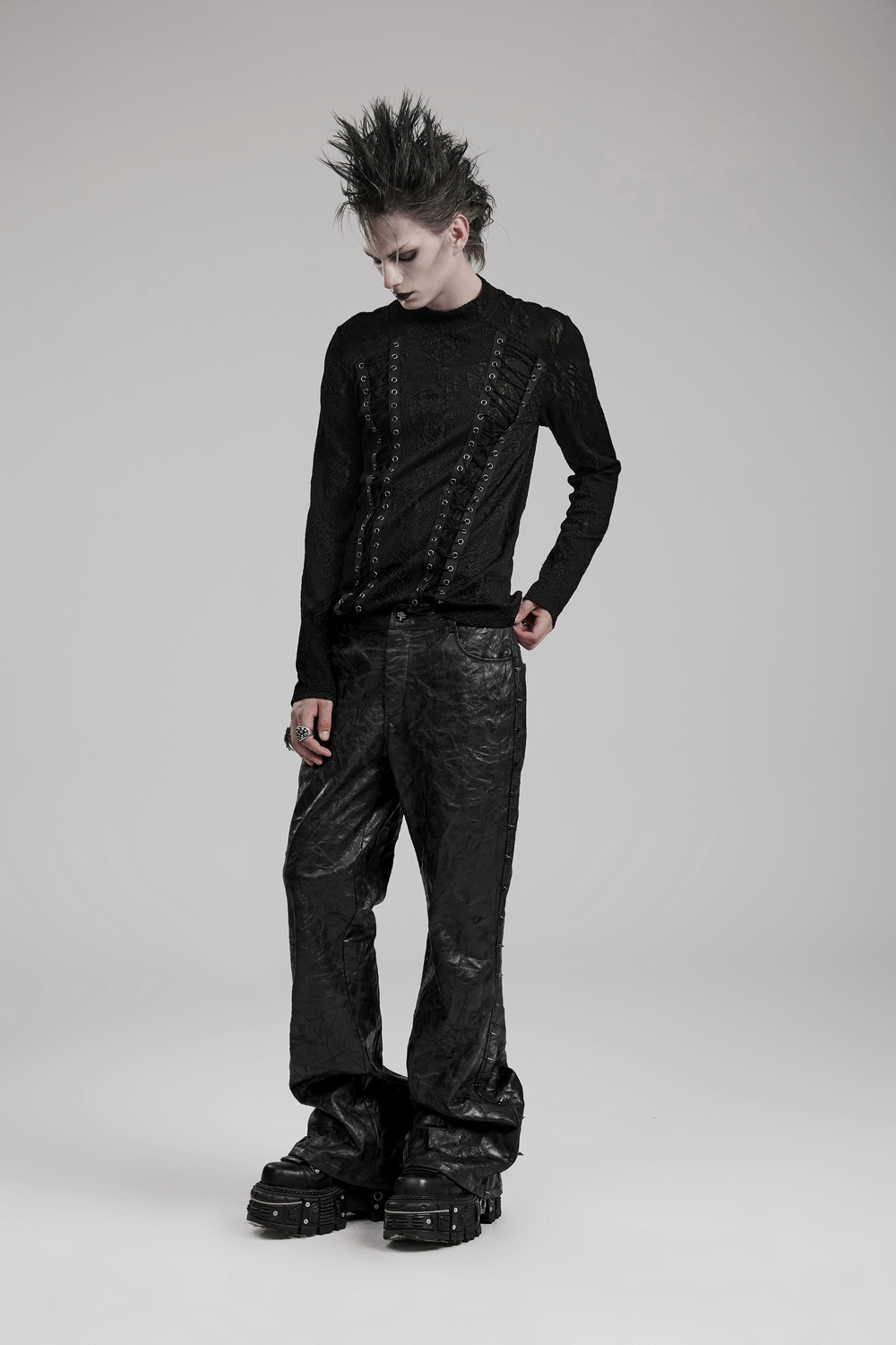Model wearing an edgy black gothic top with 3D jacquard weave and webbing detail, styled with dark pants and chunky shoes.