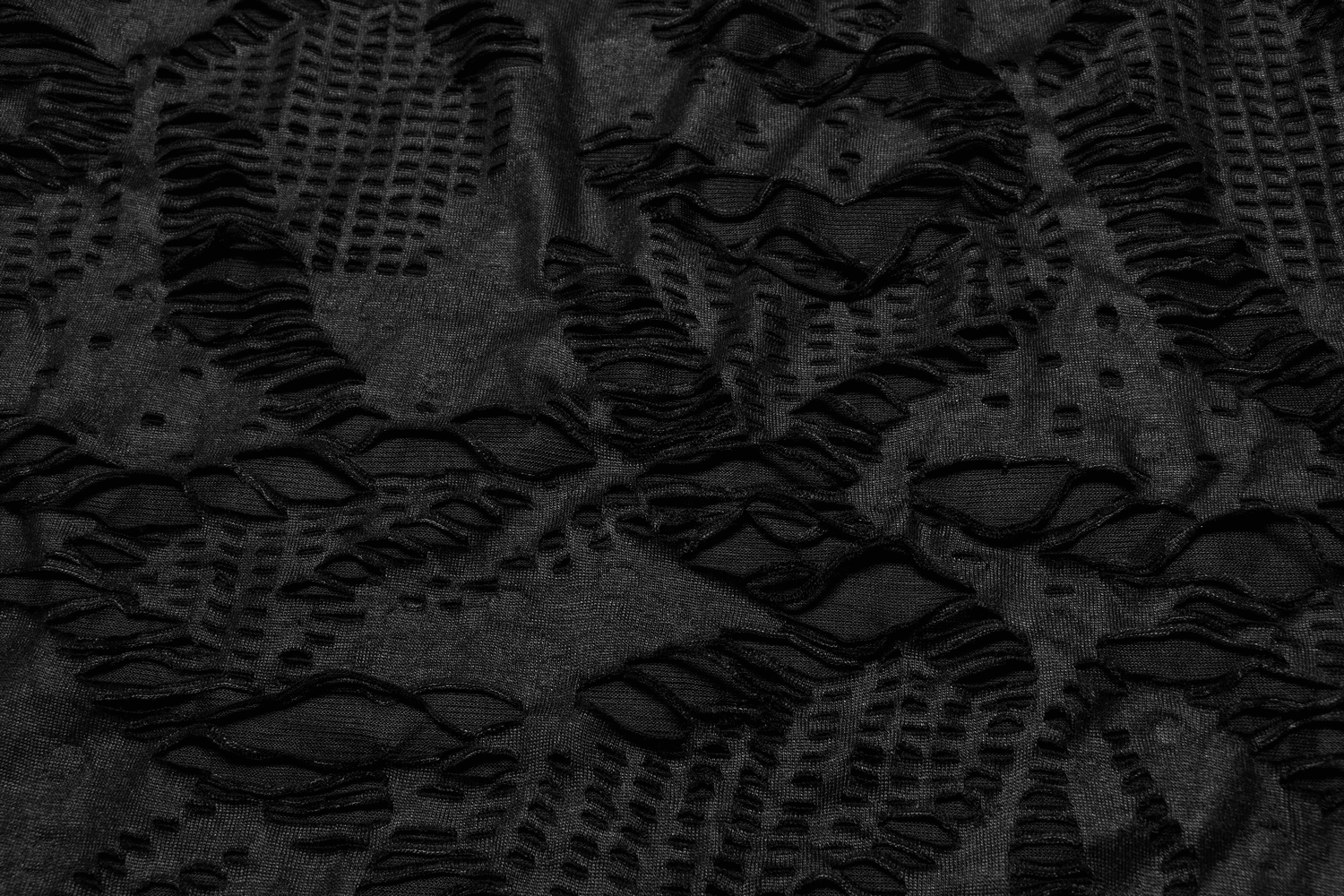 Close-up of textured black fabric featuring edgy mesh overlay and intricate hole patterns, showcasing gothic design elements.
