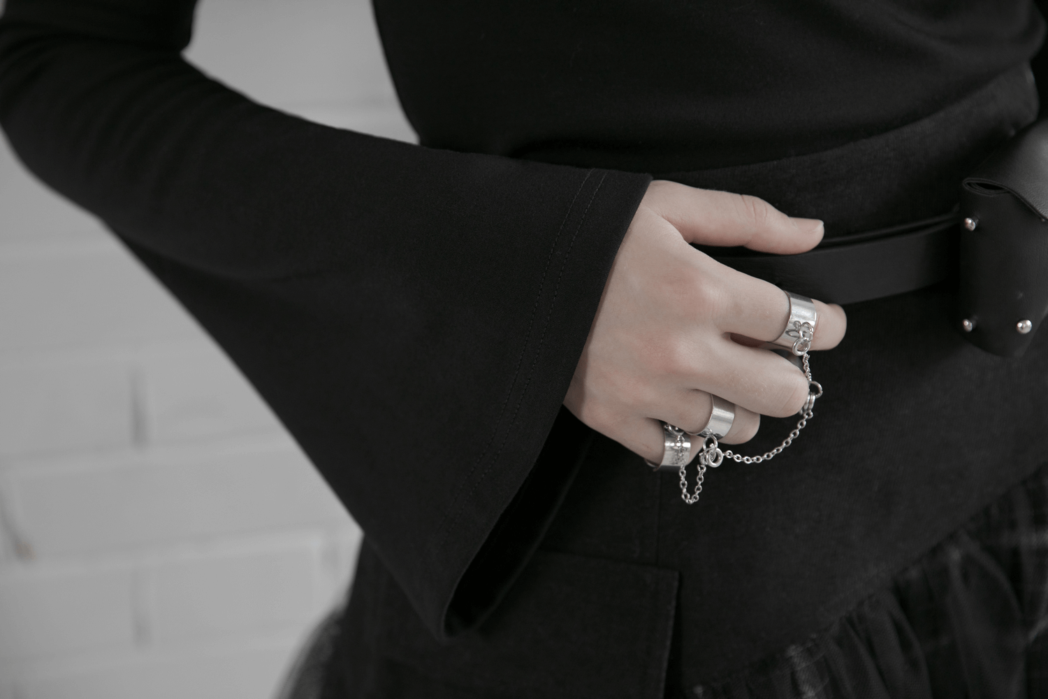 Detail of a hand with rings holding a belt on a black outfit, showcasing edgy punk style.