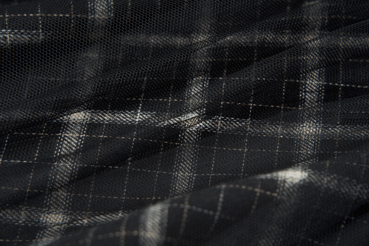 Close-up of a textured black plaid fabric with white grid pattern, featuring mesh detailing and a punk aesthetic.