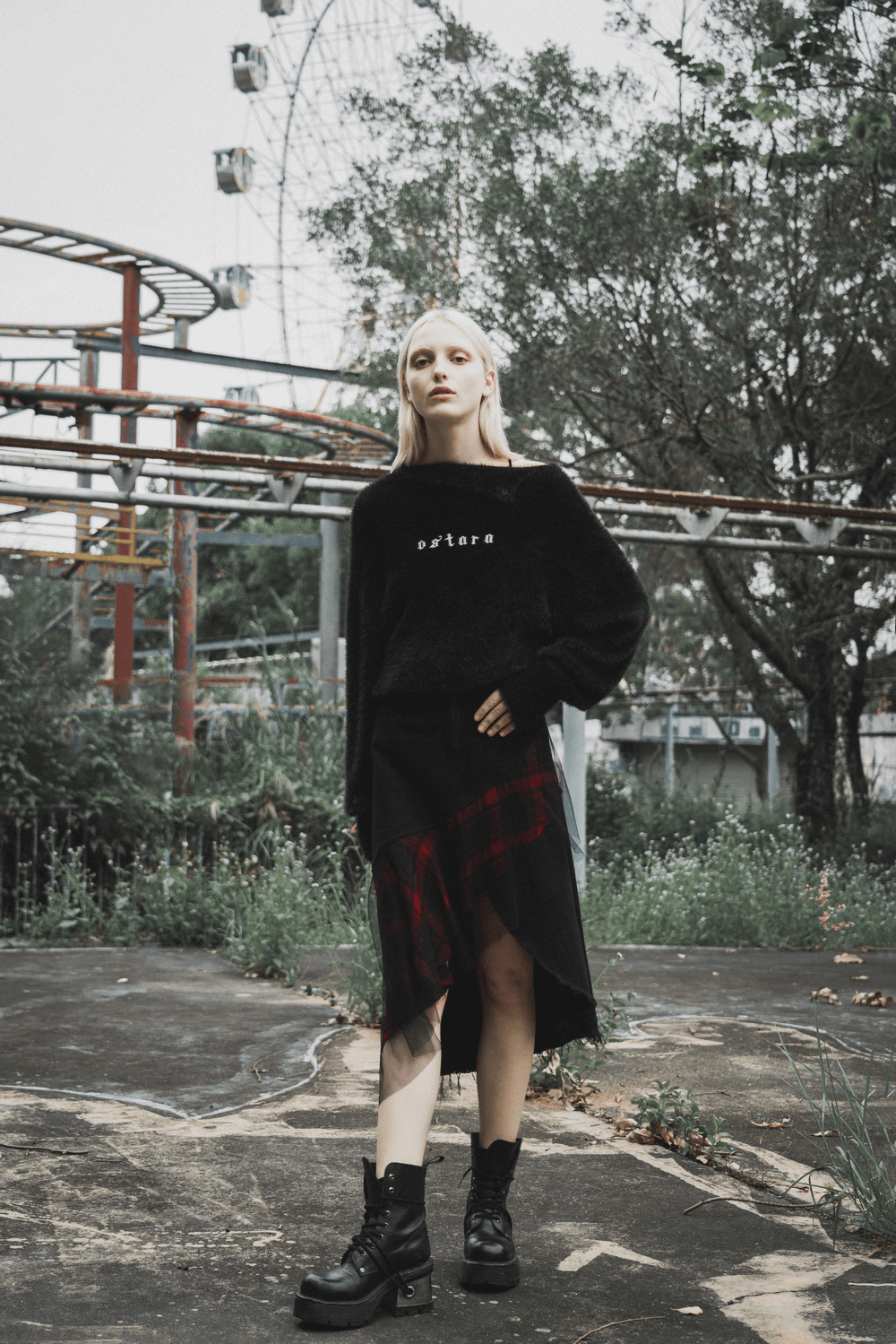 Model wearing an edgy high-waist plaid skirt with irregular hem, paired with black boots, in an urban setting.