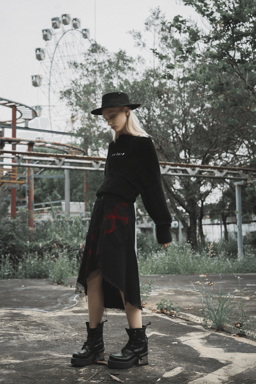 Model showing off edgy high-waist plaid skirt with irregular hem, styled with a black sweater and hat.