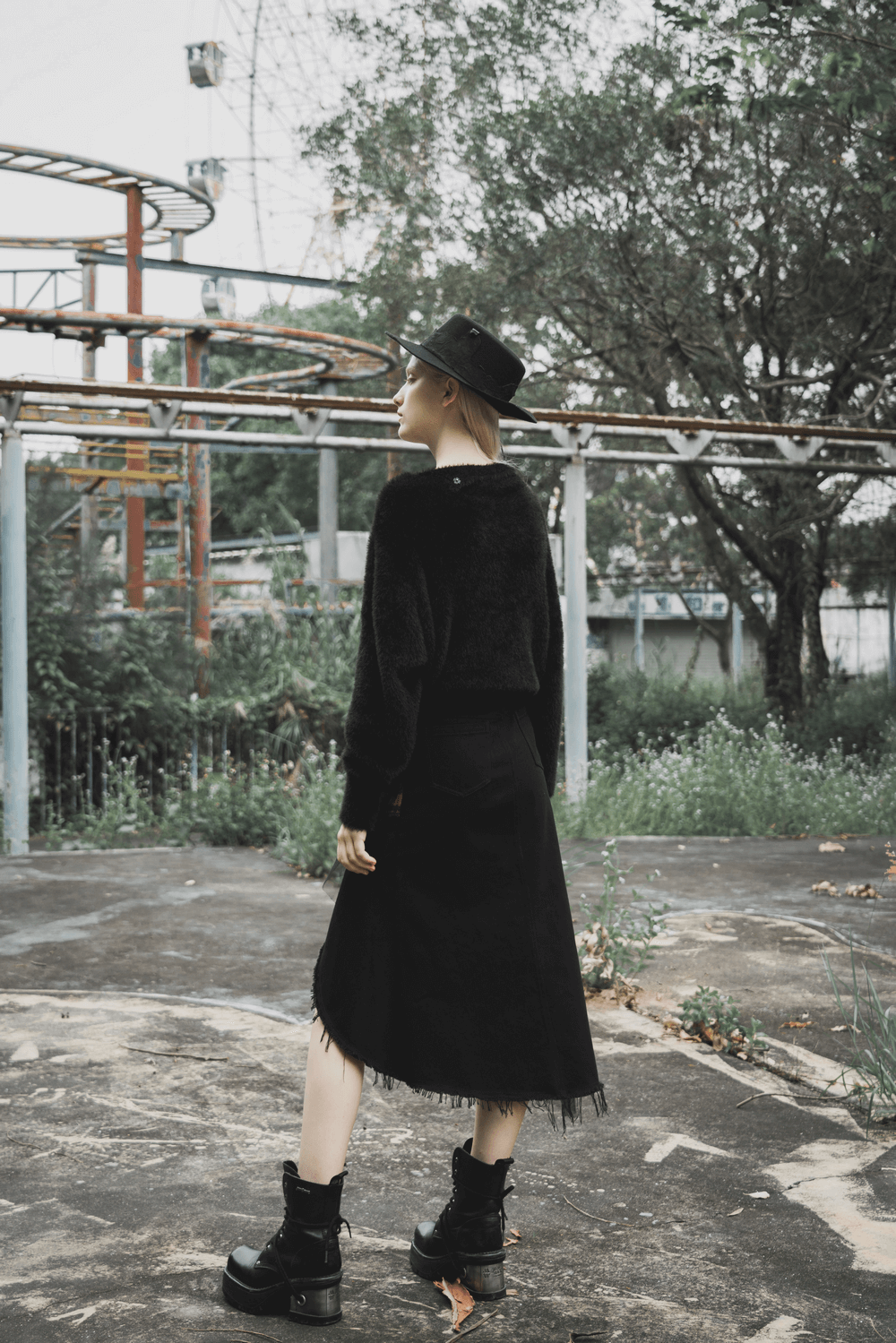 Model wearing an edgy high-waist black skirt with irregular hem, paired with a cozy sweater and stylish hat.