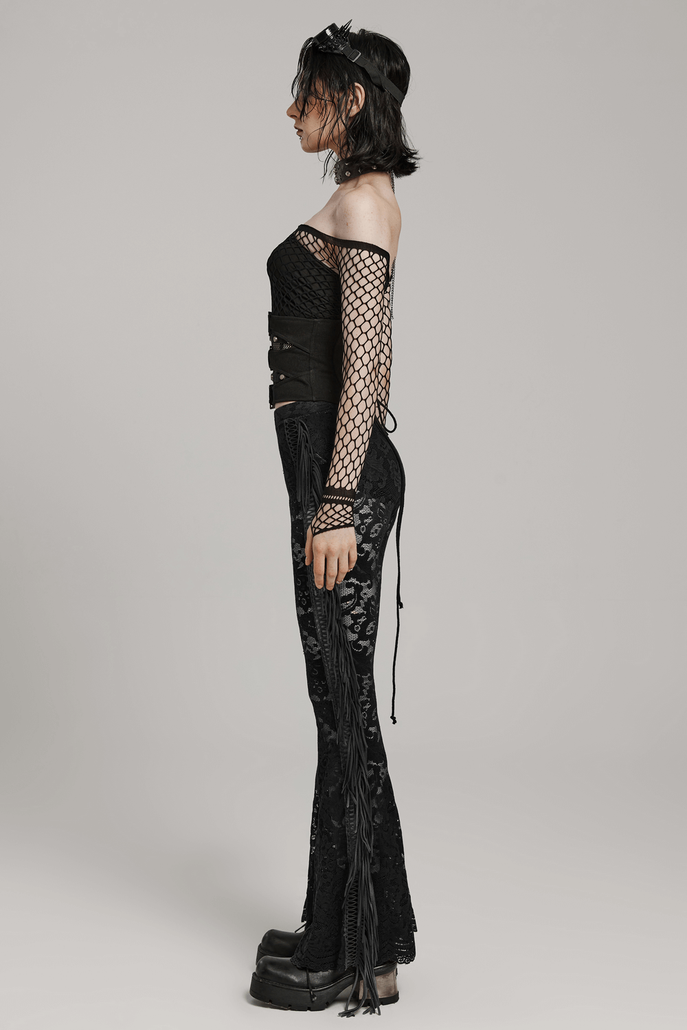 Model showcasing an edgy black corset belt outfit with fishnet sleeves and flared pants for a punk look.