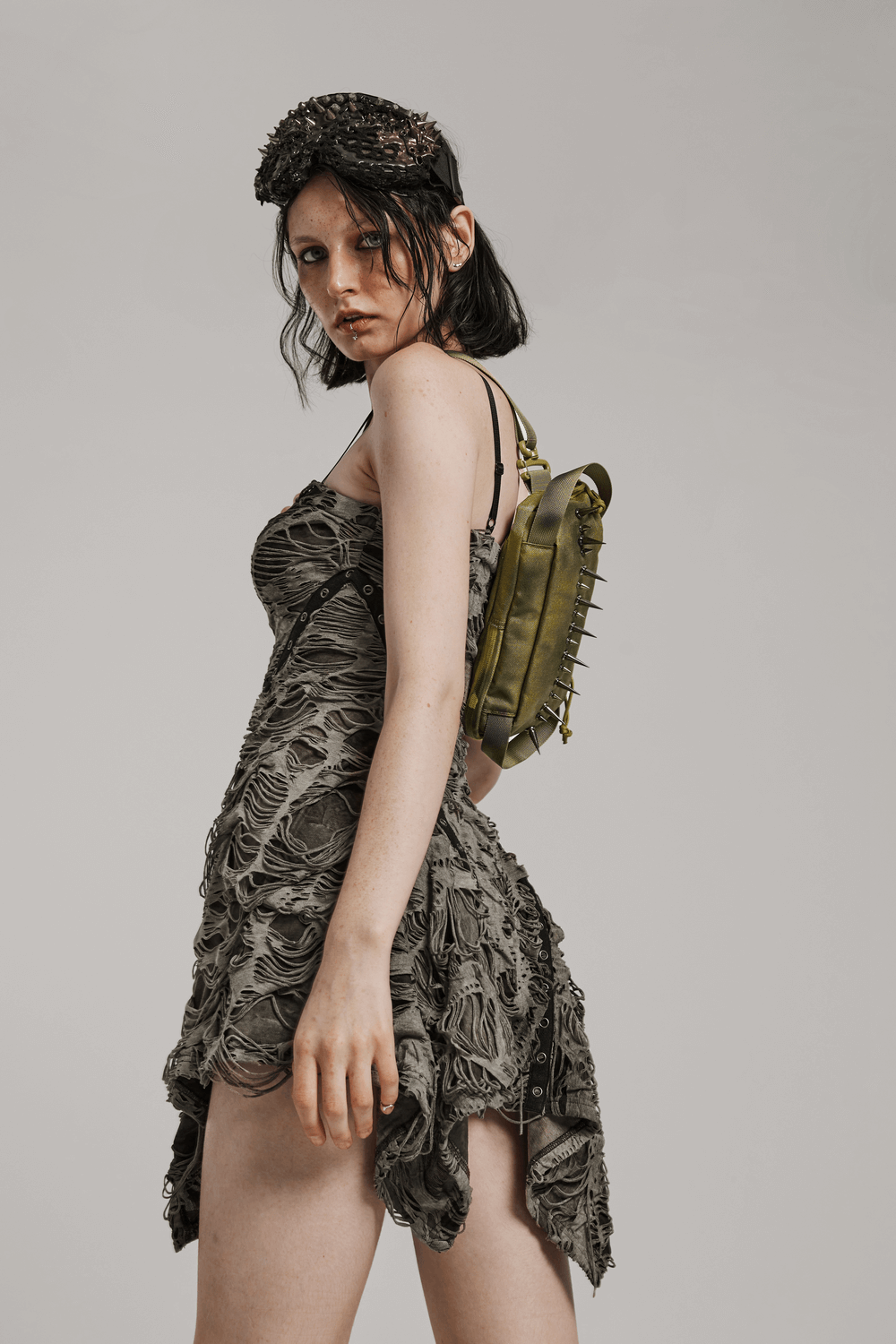 Model wearing edgy green nylon spiked shoulder bag over a textured dress for a streetwear vibe.