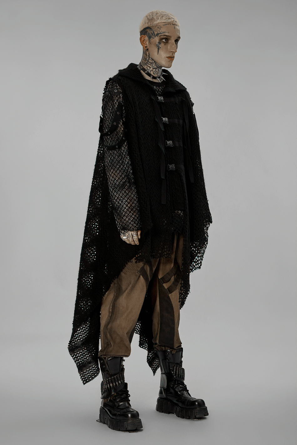 Model showcasing an edgy post-apocalyptic knitted gauze cape with webbing detail in an alternative fashion setting.