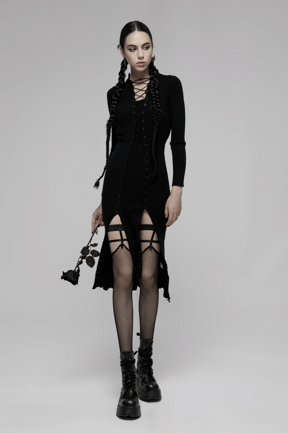 Edgy punk fashion model in black dress with fishnet socks and combat boots, holding a rose.