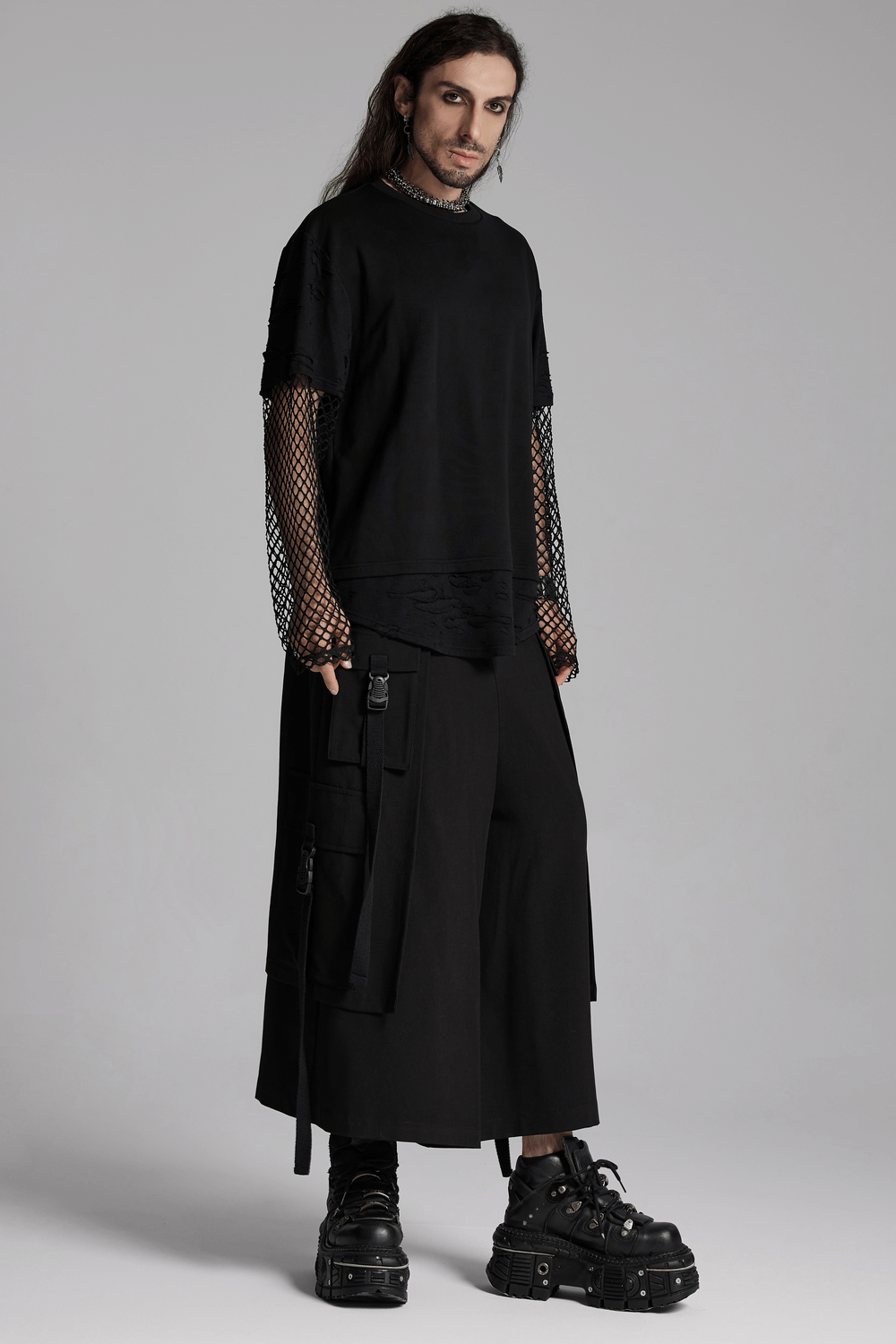 Edgy punk mesh-sleeved distressed top for men with loose fit and dropped shoulders, paired with black pants and boots.