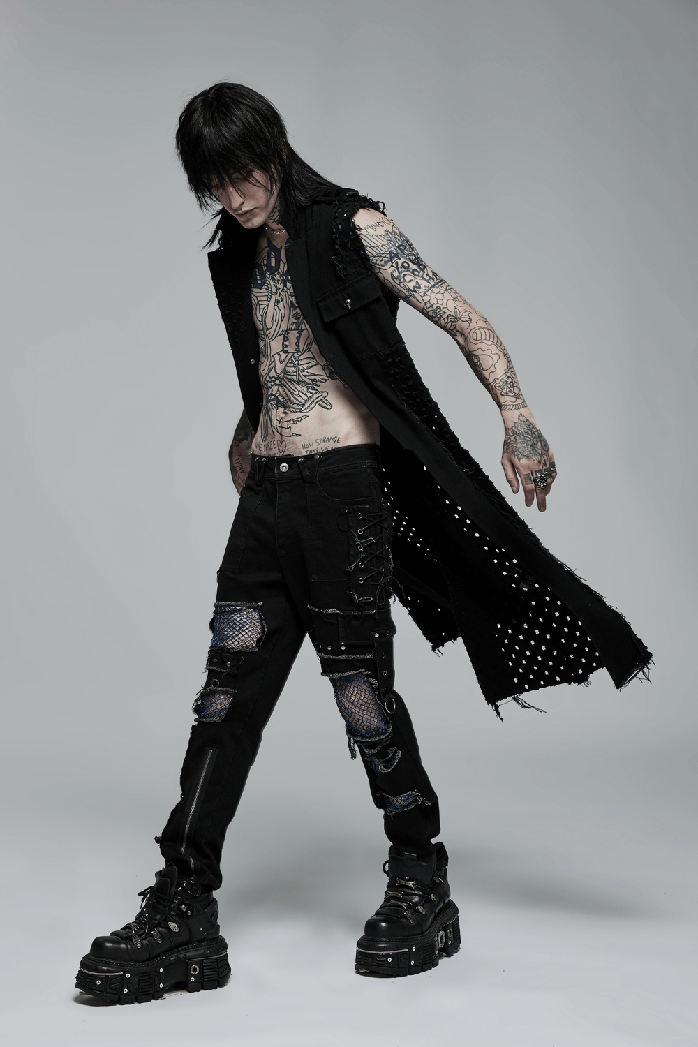 Edgy punk model in medium-length cape with distressed details and tattoos, showcasing alternative fashion vibes.