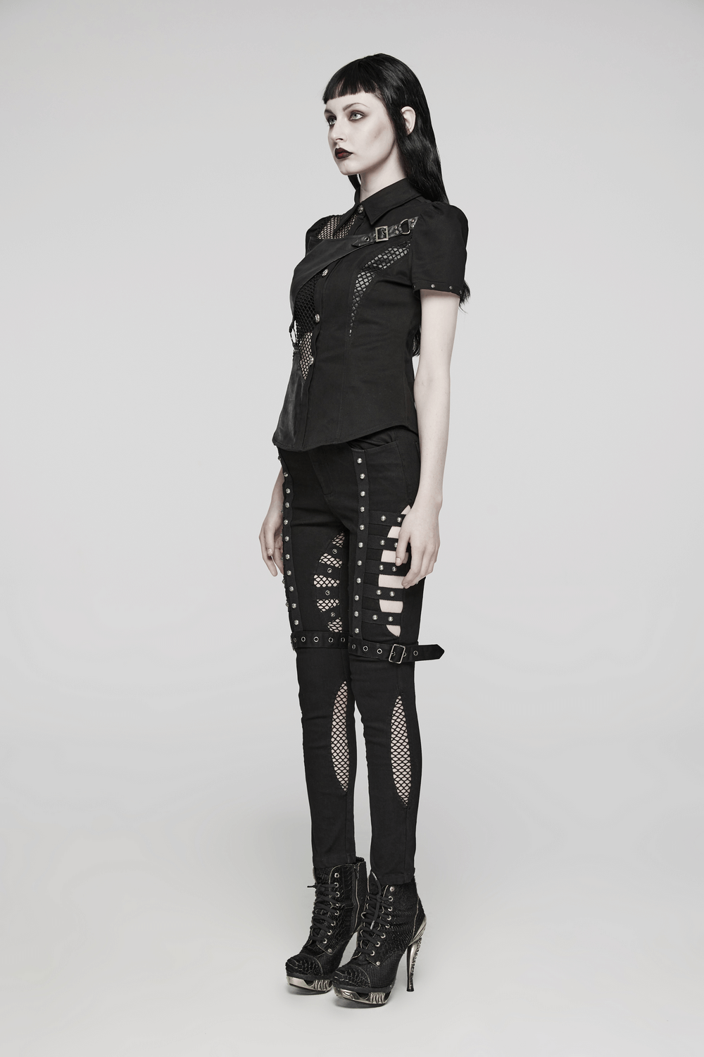 Model showcasing edgy punk riveted slim jeans with mesh panels and buckles, styled for a bold fashion statement.