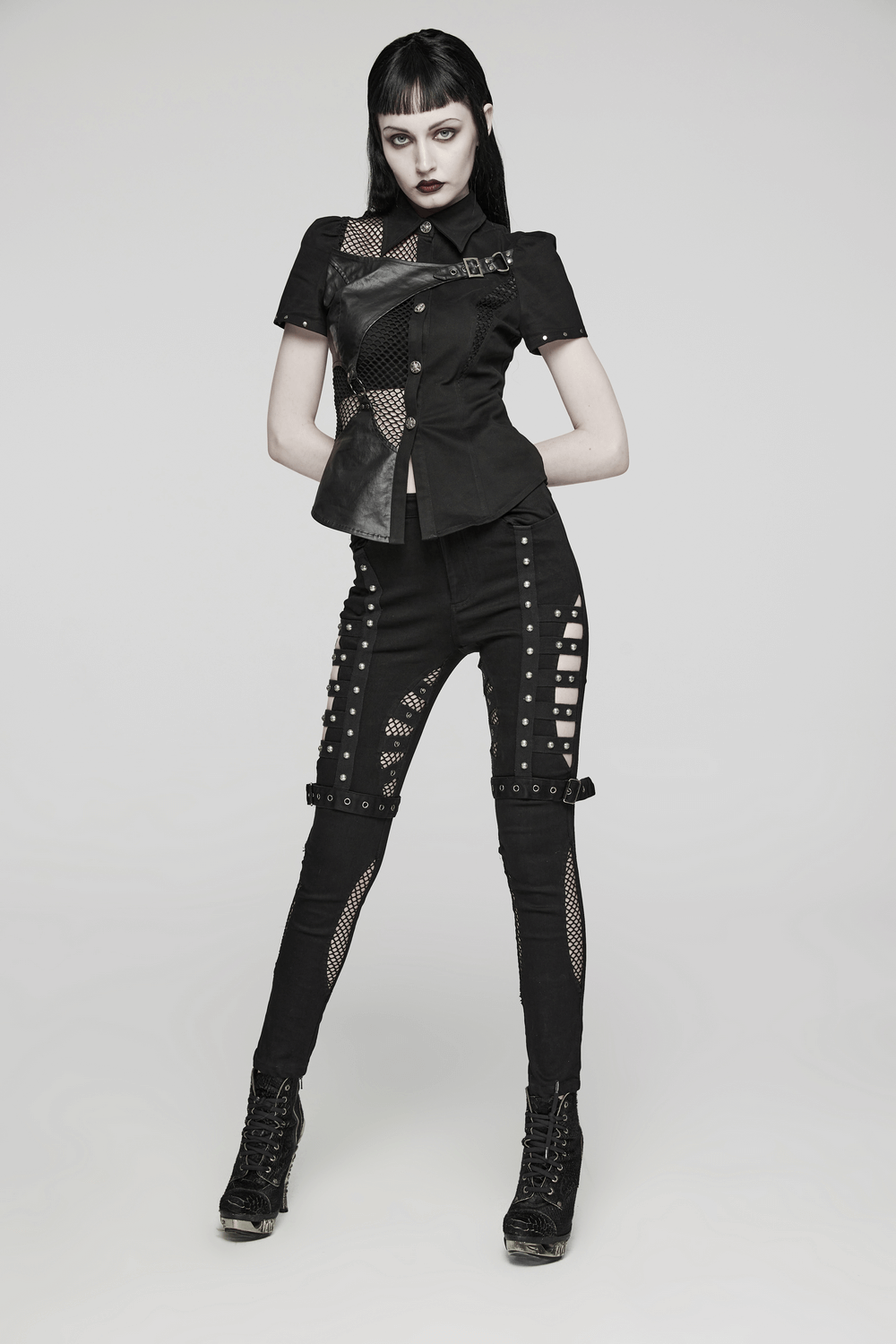 Edgy punk model wearing riveted slim jeans with mesh panels and buckles, showcasing a bold fashion statement.