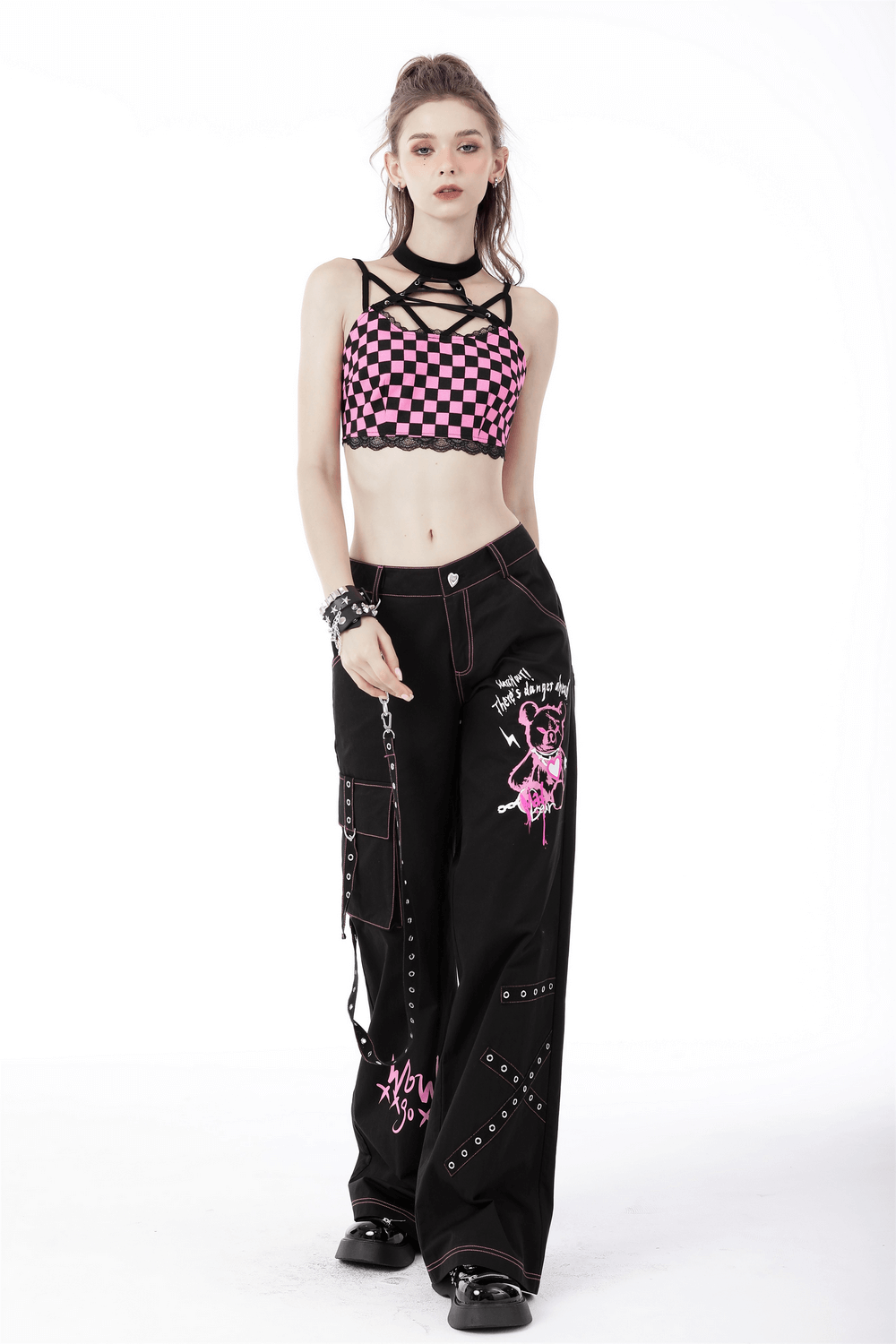 Edgy punk rock model in black wide pants with pink skull details, chains, and checkered crop top.