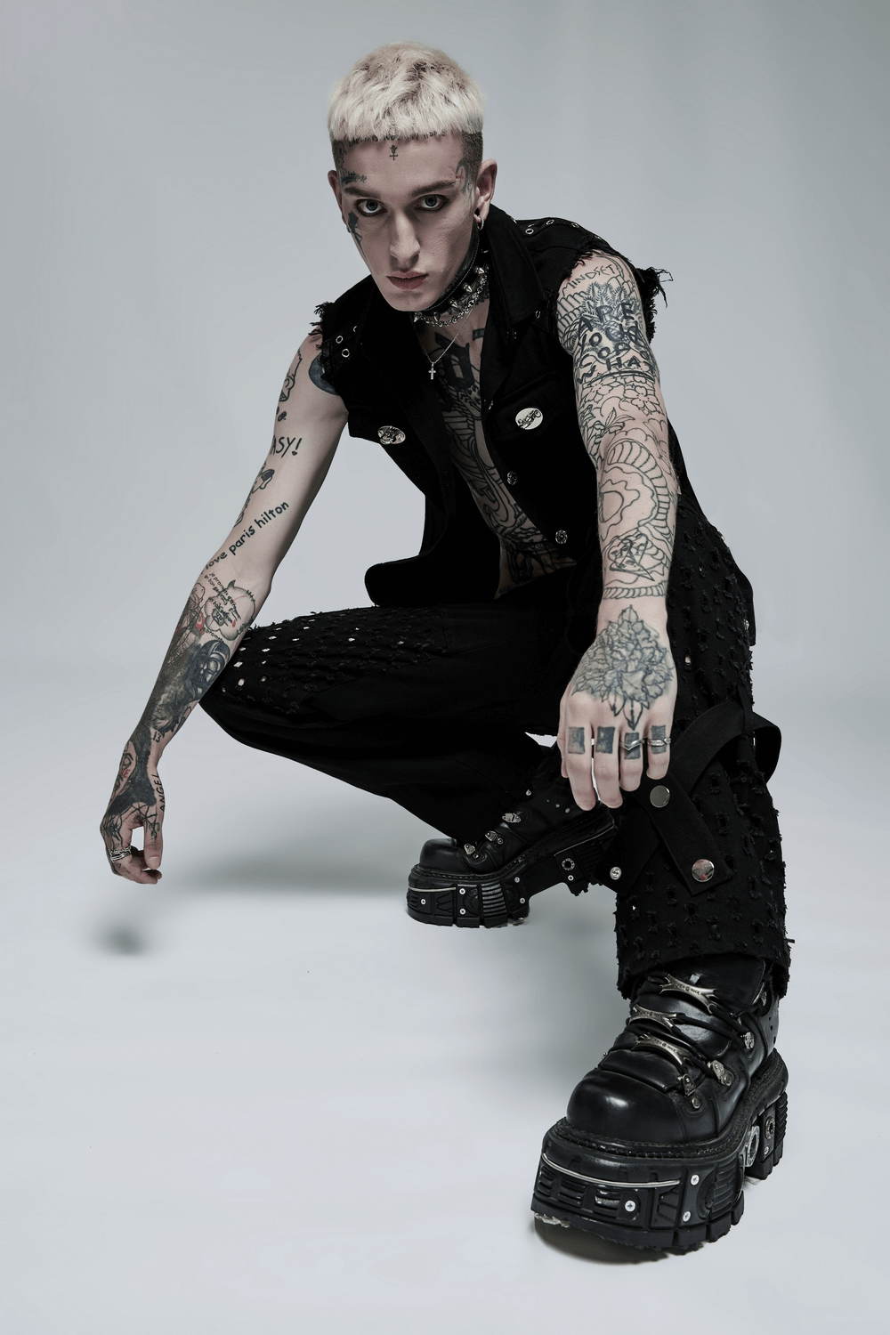 Edgy punk model in sleeveless twill vest with metal accents and tattoos, showcasing rebellious fashion style.